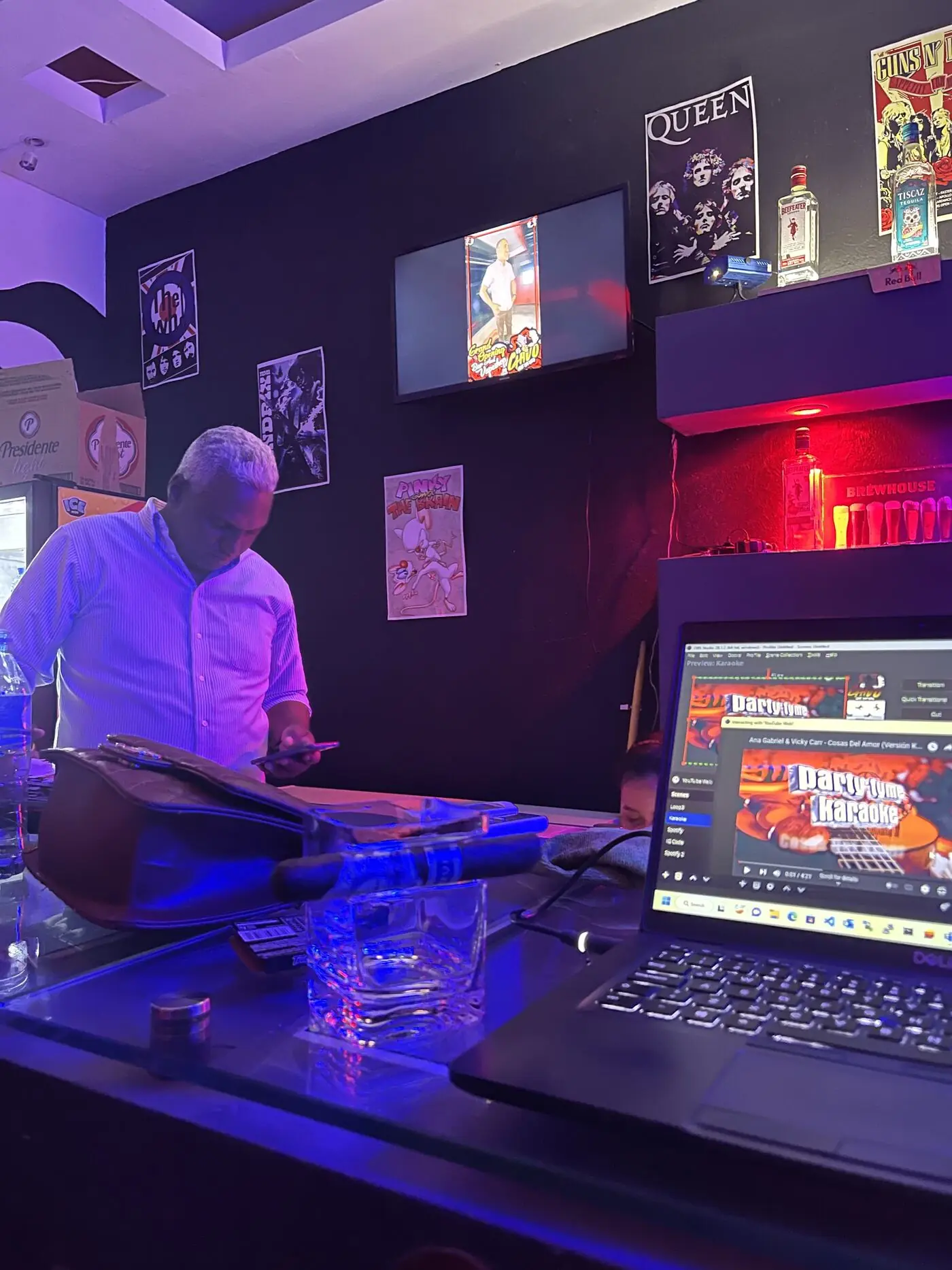 La cabina del bar alumbrada en rojo y azul, con afiches de Queen, The Who y Guns N' Roses