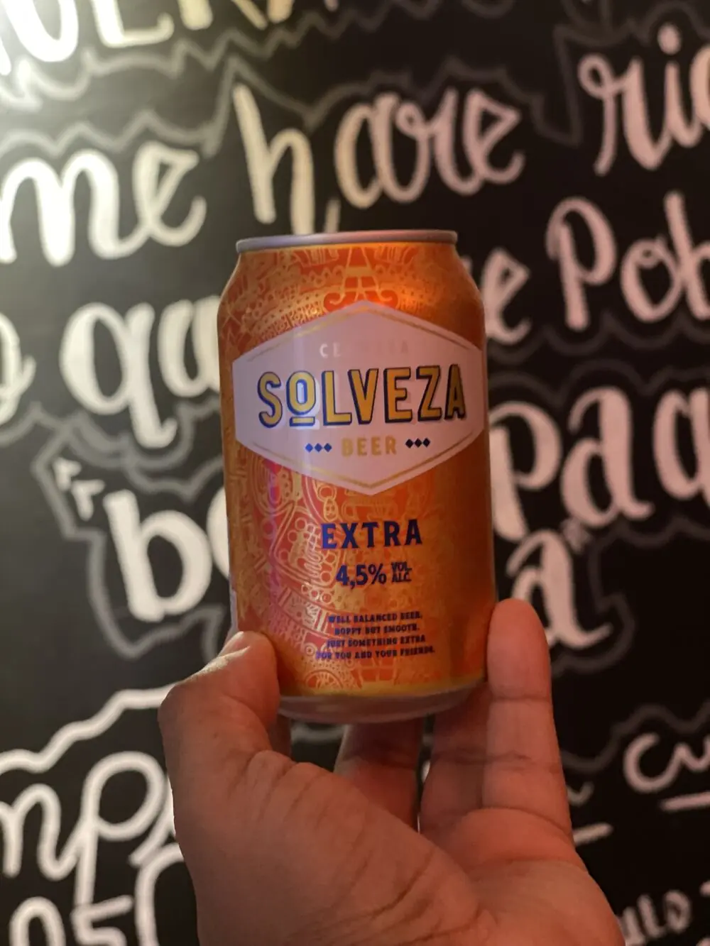 Una lata de cerveza alzada contra el lettering blanco de la pared negra