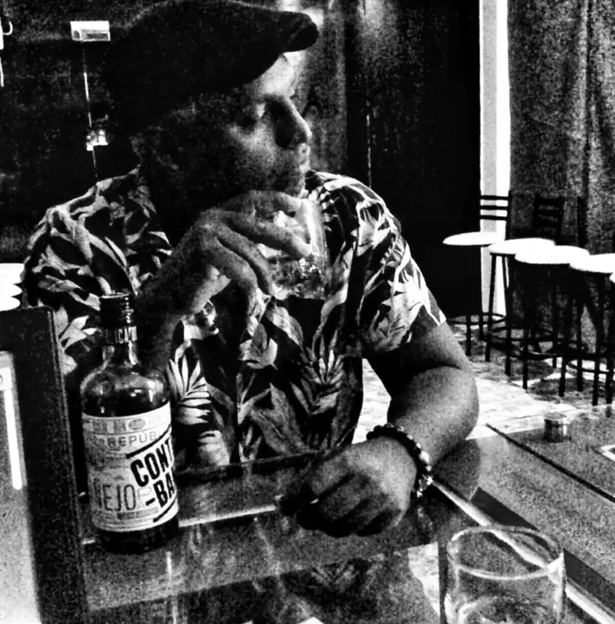 Retrato en blanco y negro de un cliente en la barra, con su botella al lado